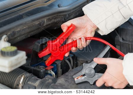 Hands connecting booster cables to a car battery