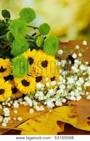 Beautiful flowers with yellow leaves on table on bright background