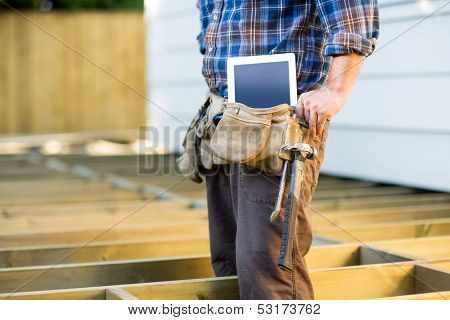Midsection of construction worker with tablet computer and hammer in toolbelt at site
