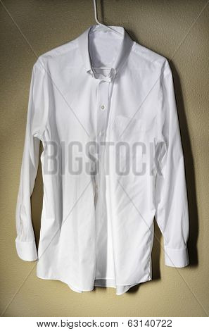 Detail of white dress shirt hanging on hanger with light