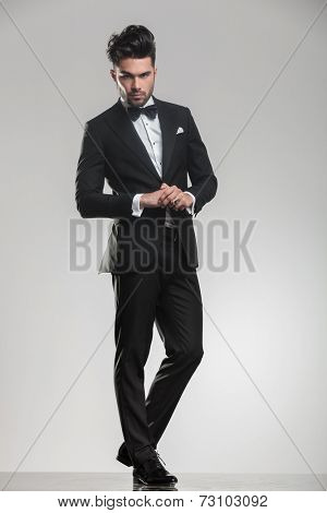 Full body picture of a elegant young man wearing a tudexo looking at the camera while holding his hands,