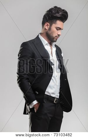 Portrait of an elegant young man in tuxedo holding his hands in pocket while looking down