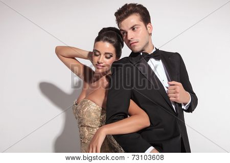 Woman wearing elegant dress holding her lover arm, looking down, while the man is ajusting his jacket.