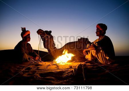 Two indigenous Indian men resting by the bon fire with their camel.
