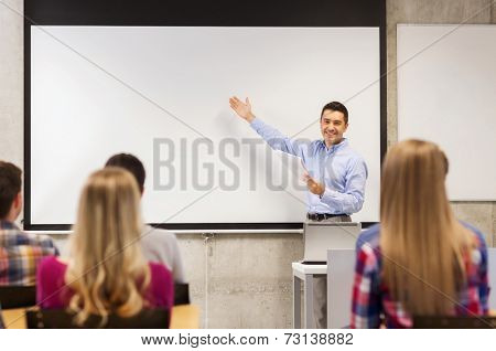 education, high school, technology and people concept - smiling teacher with notepad, laptop computer standing in front of students and showing something on white board in classroom
