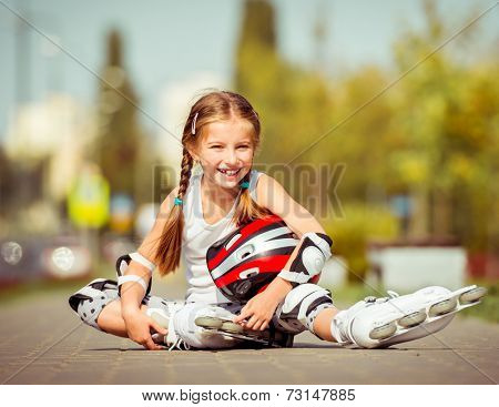 Little girl in roller skates sitting on a city street