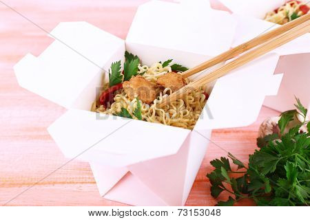 Chinese noodles with meat and pepper in takeaway box on pink background