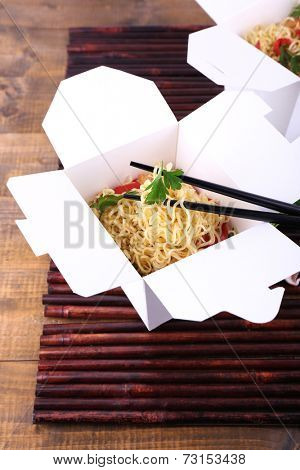 Chinese noodles in takeaway box on bamboo mat background