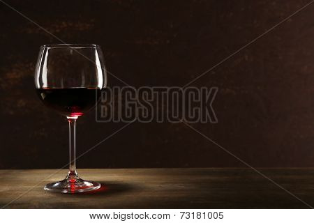 Goblet of red wine on wooden table on wooden wall background