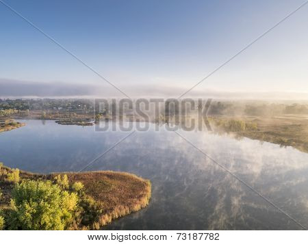 aerial view of a morning fog over lake, early fall scenery, Riverbend Ponds Natural Area, Fort Collins, Colorado, shot from low flying drone