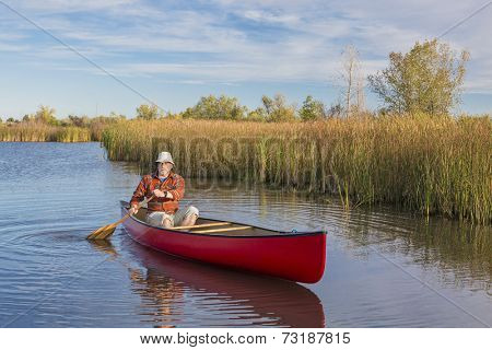 senior male paddler paddling a red canoe on a calm lake, Riverbend Ponds Natural Area, Fort Collins, Colorado