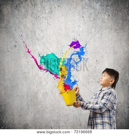 Young boy splashing colorful paint from bucket