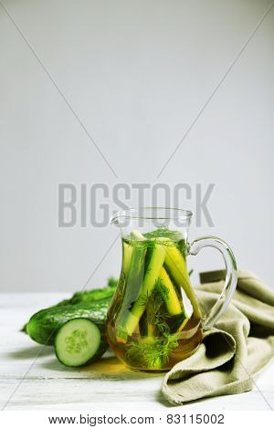 Glass ewer with fresh organic cucumber water on wooden table, on grey background