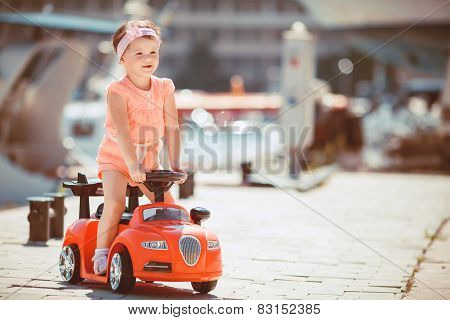 Little girl riding a children's car on the waterfront.