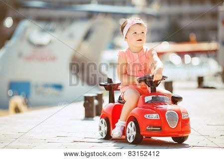 Little girl riding a children's car on the waterfront.