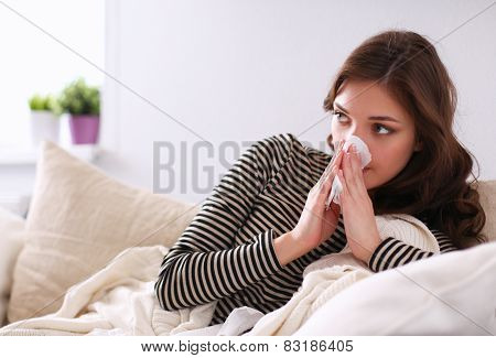 Portrait of a sick woman blowing her nose while sitting on the sofa
