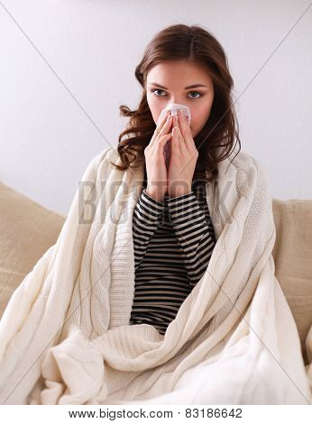 Portrait of a sick woman blowing her nose while sitting on the sofa