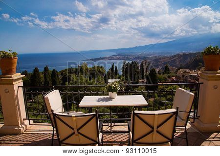 table and chairs at balcony overlooking sicilian coastline
