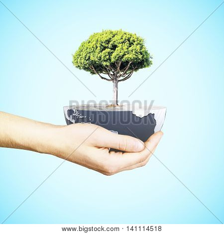 Male hand holding half a globe with large tree on blue background. Green earth concept. 3D Rendering