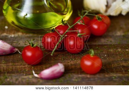 closeup of some cherry tomatoes, some garlic cloves and a glass cruet with olive oil on a rustic wooden table