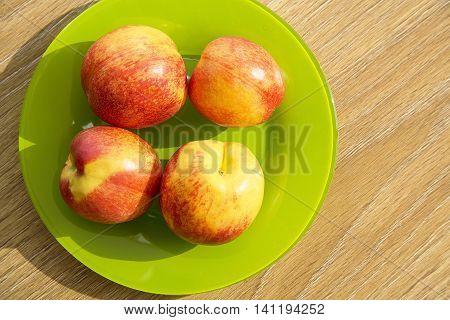Nectarines in a green plate on a wooden table