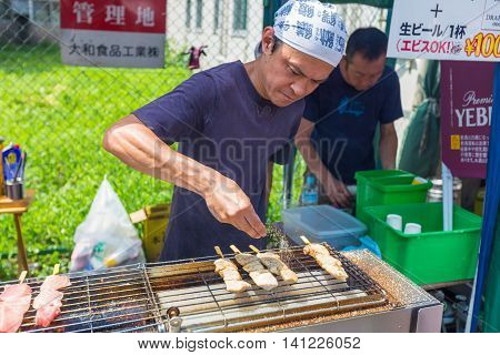 TOKYO JAPAN - 18 JULY 2016 - Street vendor man cooks fish on sticks at Tsukiji Fish Market in Tokyo Japan on July 18 2016