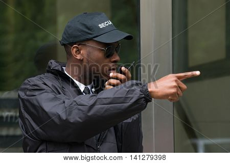 Young Male Security Guard Gesturing While Talking On Walkie-Talkie