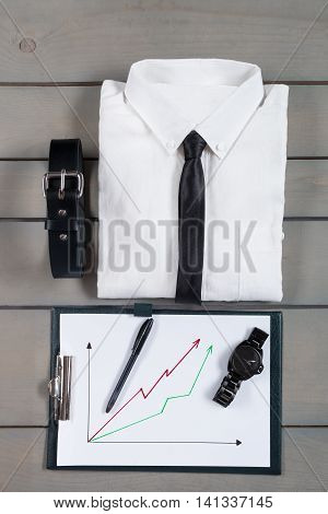 Businessman work outfit on grey wooden background. White shirt with black tie belt planchette. Back to work. Set of mans fashion and accessories. Copy space frame.