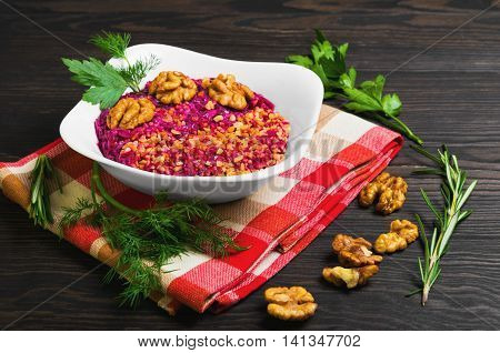Fresh vegetarian salad with beets walnuts herbs rosemary parsley fennel in white bowl on brown wooden background cloth with pattern of cell