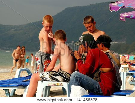Patong / Phuket Thailand - January 11 2007: Thai tattoo artist applies temporary tattoos to a family of Swedish tourists on Patong Beach