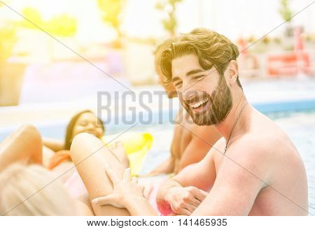 Group of friends relaxing in swimming pool party - Bearded man laughing with girl while she's lying in airbed up the water - Vacation and pool party concept - Warm vivid filter