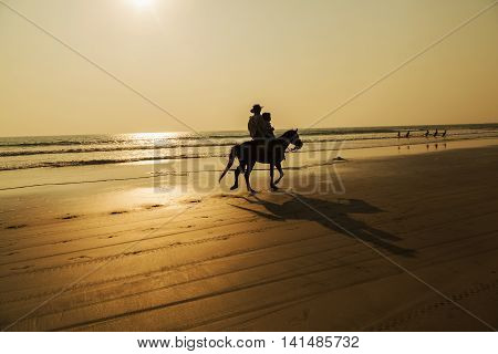 A man rides a horse on a beach with a beautiful sunset in NGWE SAUNG beach Myanmar