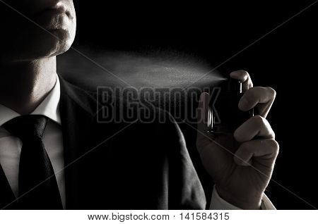Elegant man in suit and tie using cologne or perfume isolated on black