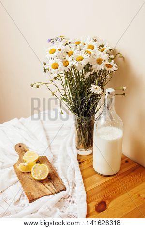 Simply stylish wooden kitchen with bottle of milk and glass on table, summer flowers camomile, healthy foog moring concept noone
