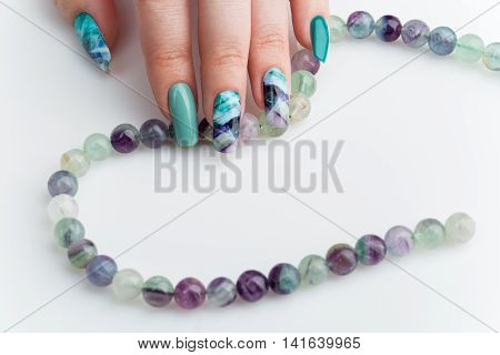 Closeup of woman nails with creative purple and green manicure. Fluorinit print. Natural stone beads. Copy space.