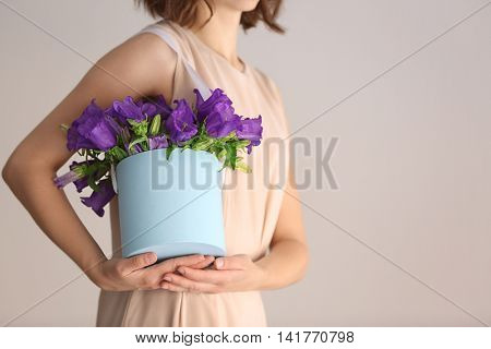Woman holding box with purple bellflowers on light background