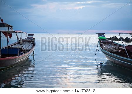 Traditional asian boats in calm sea during sunset directed towards the horizon with copy space