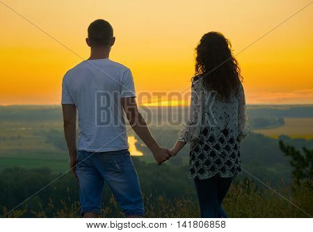 romantic couple looking into the distance at sunset on outdoor, beautiful landscape and bright yellow sky, love tenderness concept, young adult people