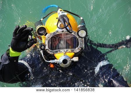 diver in the water in a diving suit and helmet ready to dive and showing sign ok