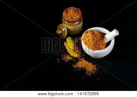 Turmeric powder in mortar with pestle and roots with clay pot on black background