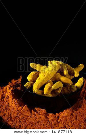 Turmeric powder and roots or barks on black background