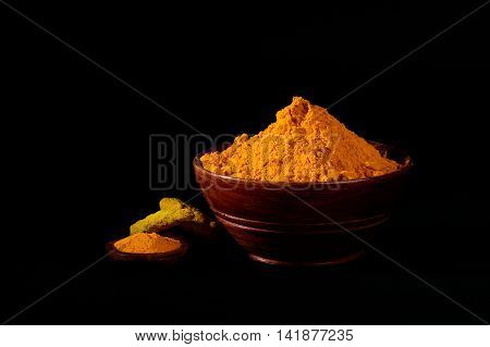 Turmeric powder and roots or sticks in wooden bowl on black background