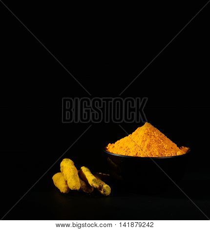 Turmeric powder and roots or barks in black bowl on black background