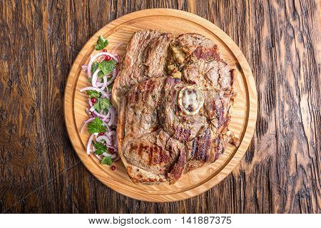 Medium rare grilled Beef steak Ribeye with onion on cutting board on dark wooden background. Top view
