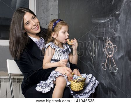 teacher with pupil in classroom at blackboard writting, mother and daughter first time to school, lifestyle people concept