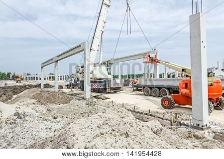 Mobile crane is operating and worker is assembly concrete joist in high place. Height worker is placing truss on building skeleton.
