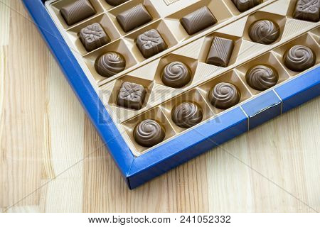 Top View On Wooden Table With Carton Of Various Shape Candies Set. Blue Package With Special Cells F