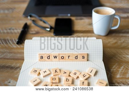 Closeup On Notebook Over Table Background, Focus On Wooden Blocks With Letters Making Adwords Word.