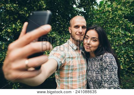 A Guy With A Girl Taking Selfies On A Green Foliage Background