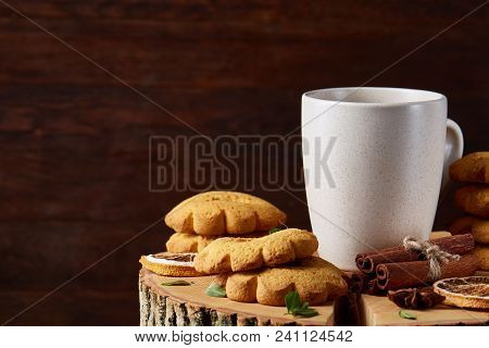 Christmas Concept With A White Porcelain Cup Of Hot Tea, A Large Set Of Cookies, Cinnamon Sticks Bun